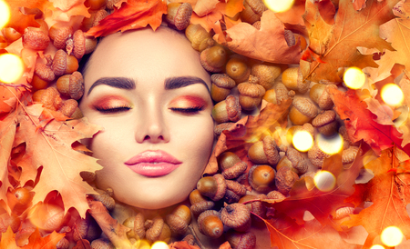 Autumn woman makeup. Beautiful autumn model girl face portrait with bright yellow, red and orange color leaves and oak acornsの写真素材