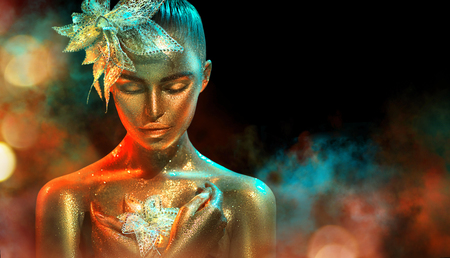 Fashion model woman in colorful bright golden sparkles and neon lights posing with fantasy flower. Portrait of beautiful girl with glowing makeupの写真素材