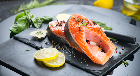 Salmon. Raw trout fish steak with herbs and lemon on black slate background. Cooking, seafoodの写真素材