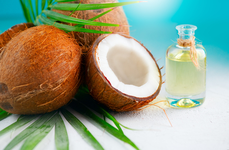 Coconut oil in a bottle with coconuts and green palm tree leaf over blue. Healthy eating. Skincare conceptの写真素材