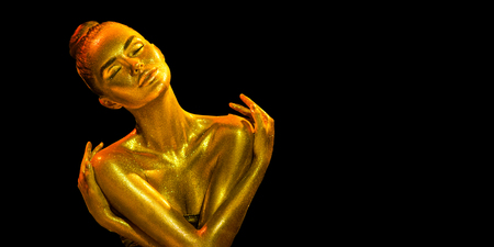 Golden skin woman portrait closeup. Sexy model girl with holiday golden shiny professional makeup. Golden metallic bodyの写真素材