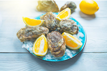 Fresh Oysters closeup on blue plate, served table with oysters, lemon and ice. Healthy sea food....
