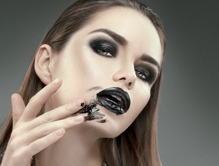 Halloween makeup. Fashion model girl with trendy gothic black make-up. Young woman smears black lipstick on her faceの写真素材
