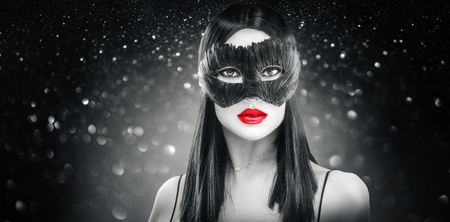 Beauty glamour brunette woman wearing carnival feather dark mask, party over holiday glowing black backgroundの写真素材