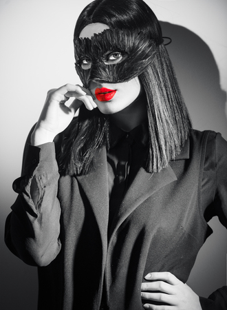 Beauty sexy brunette woman portrait. Girl wearing carnival black feather mask. Black hair, red lips, holiday makeup. Black and white fashion portraitの写真素材