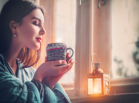 Beautiful brunette girl drinking coffee at home, looking out the window.