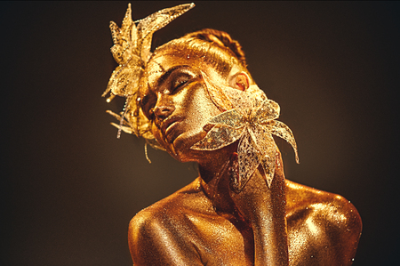 Fashion gold model woman with bright golden sparkles on skin posing, fantasy flower.の写真素材