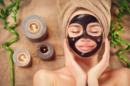 Beautiful woman with black purifying black mask on her face. Beauty model girl with black facial peel-off mask lying in spa salon. Skincare, cleansingの写真素材