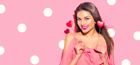 Valentine's Day. Beauty surprised young fashion model girl with Valentine heart shaped cookies isolated on pink backgroundの写真素材