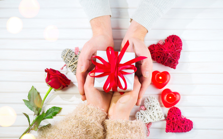 Valentine's Day. Young couple hands holding gift box over white wooden background. Love concept. Top view, flatlayの写真素材