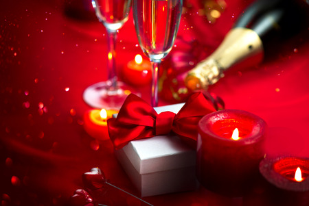 Valentine's Day romantic dinner. Date. Champagne, candles and gift box over holiday red backgroundの写真素材