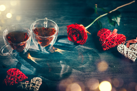 St. Valentine's Day scene. Valentine heart shaped tea cups with red hearts rattan decor and red rose on wooden background. Datingの写真素材