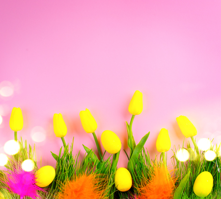 Easter background. Bright yellow eggs and vivid spring blooming tulip flowers and fresh grass over pink background. Easter backdropの写真素材