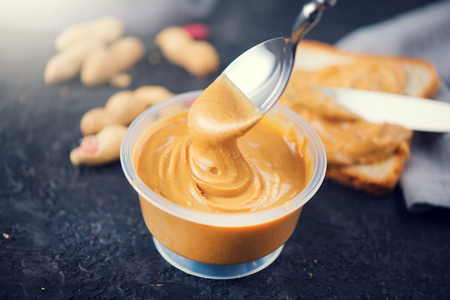 Peanut butter. Creamy smooth peanut butter in a jar on a table. Spoon of Natural nutrition. Organic foodの写真素材
