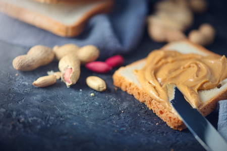 Peanut butter. Person making peanut butter sandwiches, healthy food. Woman smears butter with a knife. Natural nutrition and organic food. American cuisineの写真素材