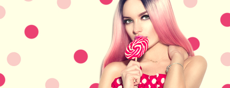 Beauty sexy model woman with pink hairstyle and beautiful makeup holding lollipop candy over polka dots backgroundの写真素材