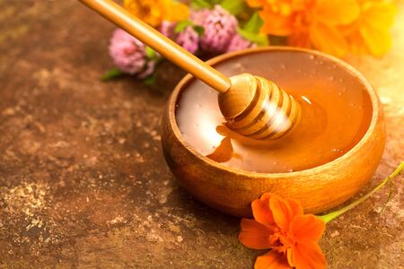 Honey dripping from honey dipper in wooden bowl. Healthy organic thick honey pouring from the wooden honey spoon closeupの写真素材