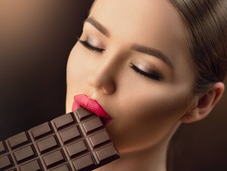 Beautiful young woman eating dark chocolate. Beauty model girl enjoying chocolateの写真素材