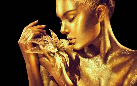 Fashion model woman with bright golden sparkles on skin posing, fantasy flower.の写真素材