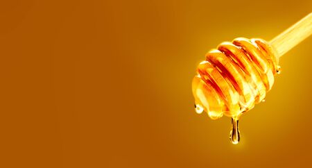 Honey dripping from honey dipper over yellow background. Thick honey dipping from the wooden honey spoon. Dieting conceptの写真素材