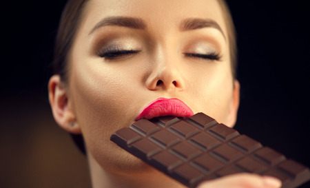 Beautiful young woman eating dark chocolate. Beauty model girl enjoying chocolateの写真素材