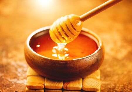 Honey dripping from honey dipper in wooden bowl. Healthy organic thick honey pouring from the wooden honey spoon closeupの写真素材