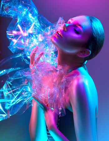 Fashion model woman in colorful bright neon lights posing in studio through transparent film. Portrait of beautiful sexy girl in UV. Art design colorful makeupの写真素材