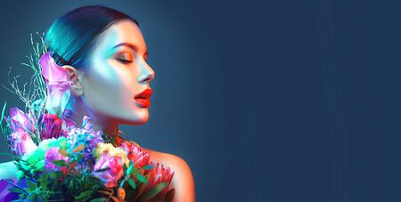 Sexy brunette model girl with bouquet of beautiful flowers. Beauty young woman with bunch of flowers in colorful neon lights. Art designの写真素材