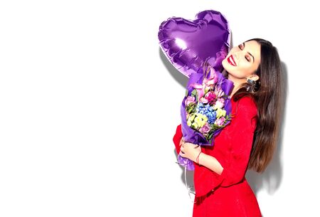 Valentine's Day. Beauty girl with colorful bouquet of flowers and heart shape air balloon on white background. Beautiful happy young womanの写真素材