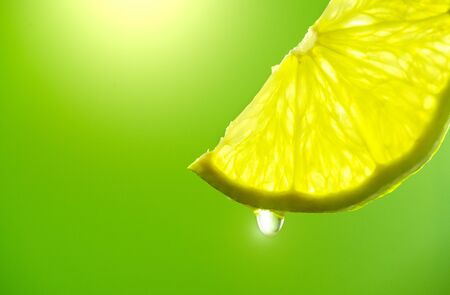 Lemon slice with drop of juice closeup. Fresh and juicy Lime over green background. Lemonadeの写真素材