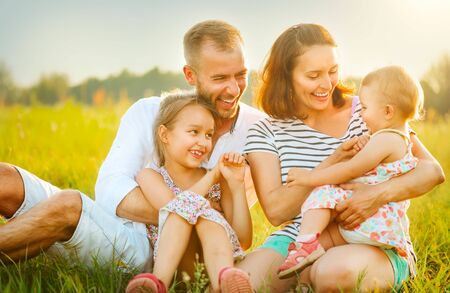 Happy joyful family. Young parents and they little kids having fun outdoors on a field