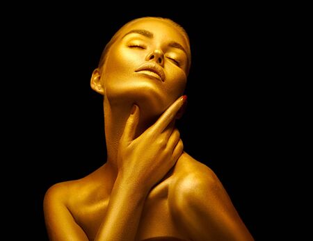 Model girl with shiny golden professional makeup over black. Beauty sexy woman with golden skin. Fashion art portrait closeup. Gold jewelleryの写真素材