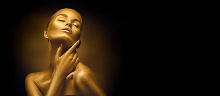 Model girl with shiny golden professional makeup over black. Beauty sexy woman with golden skin. Fashion art portrait closeup. Gold jewelleryの写真素材