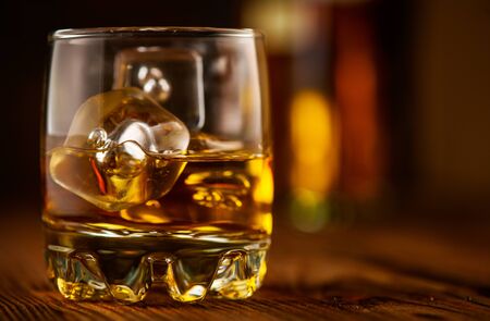Whiskey with ice cubes. Glass of Whisky and the bottle on wooden table over dark background. Glass of rum alcohol close-up. Cognac closeup, Spirits drink, cocktailの写真素材