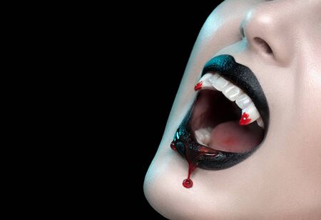 Vampire teeth with dripping blood, Woman's black bloody lips close-up. Vampire girl fangs. Fashion Halloween art design. Close up of female vampire mouth, teeth. Isolated On black backgroundの写真素材