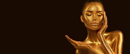 Fashion art Golden skin Woman face portrait closeup. Model girl with holiday golden Glamour shiny makeup. Sequins. Gold jewellery, jewelry, accessories. Beauty gold metallic body, Lips and Skinの写真素材