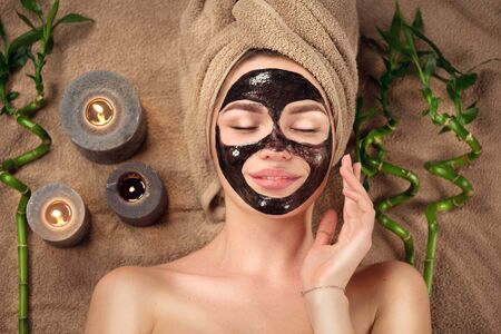 Beautiful woman with black purifying black charcoal mask on her face. Beauty model girl with black facial peel-off mask lying in spa salon. Skin care, acne treatment, cleansing skin. Peel. Top viewの写真素材