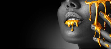 Gold Paint smudges drips from woman face, lips and hand, lipgloss dripping from sexy lips, golden liquid drops on beautiful model girl's mouth, gold metallic skin make-up. Beauty woman makeup close upの写真素材