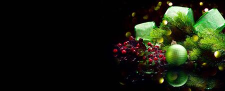 Christmas Decoration isolated on black. Wide screen backdrop. Border art design with holiday baubles. Beautiful Christmas tree closeup decorated with ball, holly berry, green ribbon. Xmas art designの写真素材