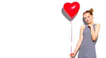 Beauty girl with red heart shaped air balloon laughing over whiteの写真素材