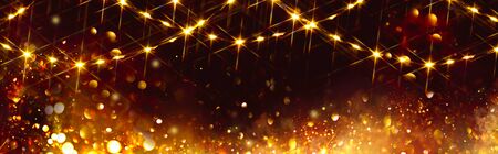 Golden Christmas and New Year glittering stars swirl on black bokeh background, backdrop with sparkling golden stars, holiday garland, magic glowing lights. Gold Abstract Glitter Blinking sparksの写真素材