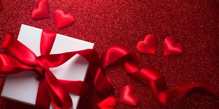 Valentine's Day Romantic Background with gift box and satin hearts. Date. Table setting with gift box over holiday red glittering background with hearts. Wedding celebratingの写真素材