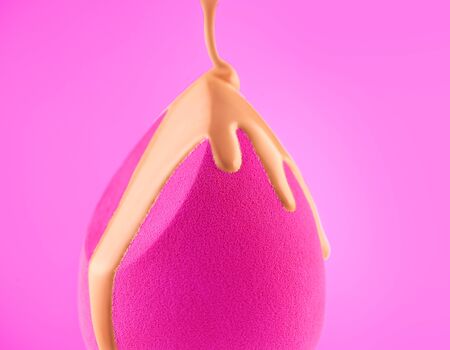 Makeup liquid foundation pouring on make-up blender sponge, closeup. Foundation beauty facial cosmetics, tool for perfect make up. Dripping bb cream or concealer, over pink backgroundの写真素材
