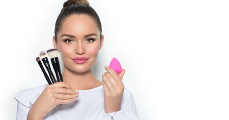 Beauty model girl, makeup artist holding set of make up brushes and sponge. Beautiful brunette young woman with perfect skin and nude make-up closeup. Face contouring. Isolated on white backgroundの写真素材
