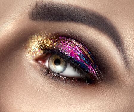 Beautiful Eye Make-up with colorful sparks. Beauty bright fashion holiday smoky eye makeup. Make up sample, close-up of model woman green color eye. Purple and golden glitter eyeshadowsの写真素材