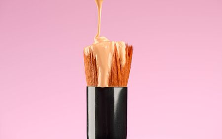 Makeup liquid foundation pouring on make-up Kabuki brush, contouring. closeup. Foundation beauty facial cosmetics, tool for perfect make up. Dripping bb cream or concealer, over pink backgroundの写真素材
