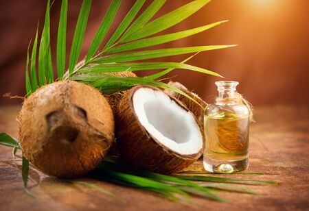 Coconut palm oil in a bottle with coconuts and green palm tree leaf on brown background. Coco nut closeup. Healthy Food, skin care concept. Vegan food. Skincare treatments. Aromatherapyの写真素材