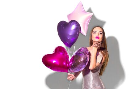 Valentine Beauty girl with colorful air balloons sending air kiss, isolated on background. Beautiful Young woman. holiday party. Joyful model having fun, playing and celebrating with colourful balloonの写真素材