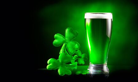St. Patrick's Day Green Beer pint over dark green background, decorated with shamrock leaves. Patrick Day Irish pub party, celebrating. Glass of Green beer close-up. Border art design, Wide formatの写真素材