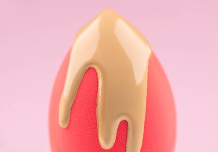 Makeup liquid foundation pouring on pink make-up blender sponge, closeup. Applying Foundation beauty facial cosmetics, tool for perfect make up. Dripping bb cream or concealer, on pink background.の写真素材